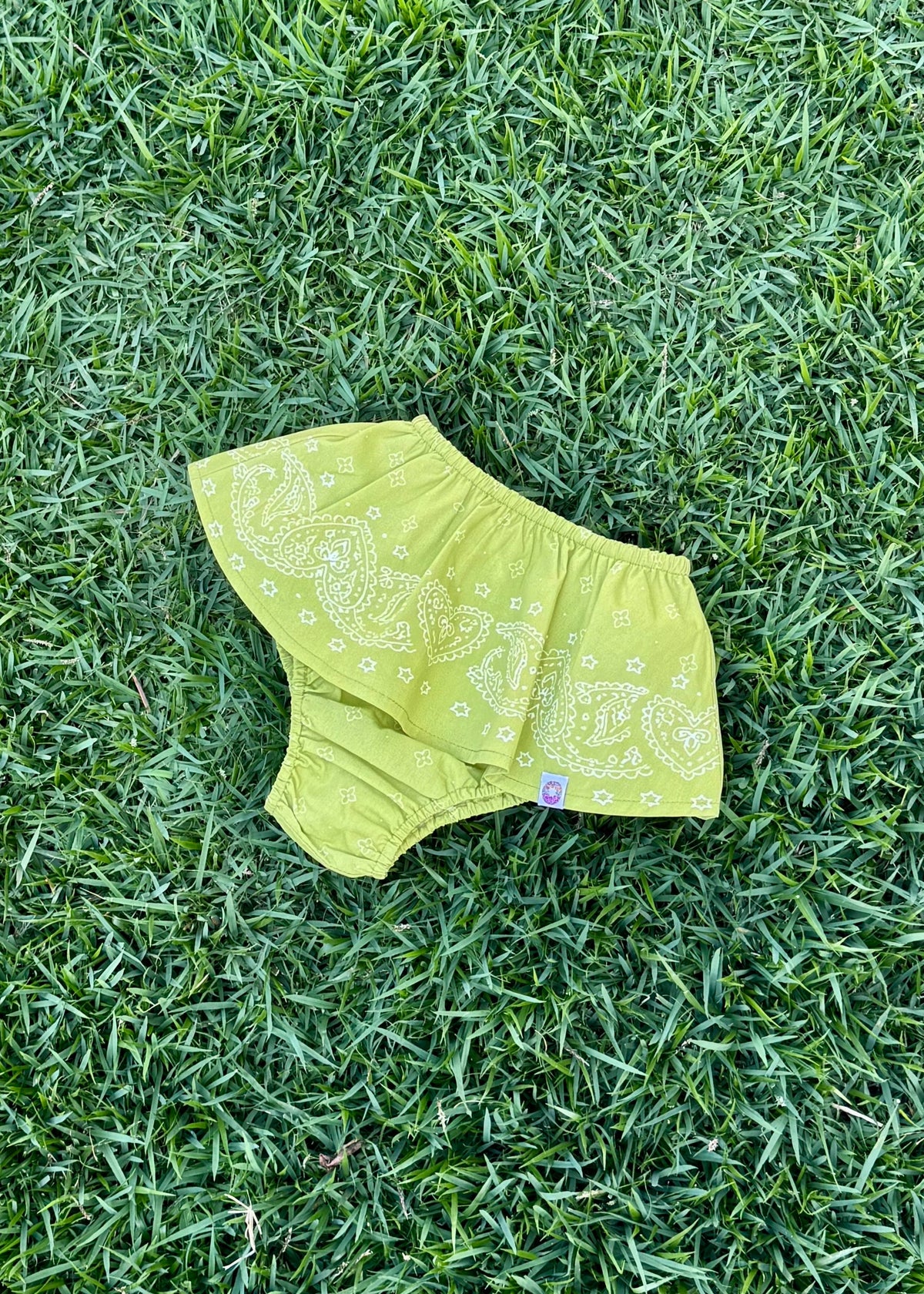 SOZO LAND Mini Bloomer in Lime green, featuring our signature Star Paisley print, a playful peplum skirt and built-in bloomers, photographed flat on green grass.
