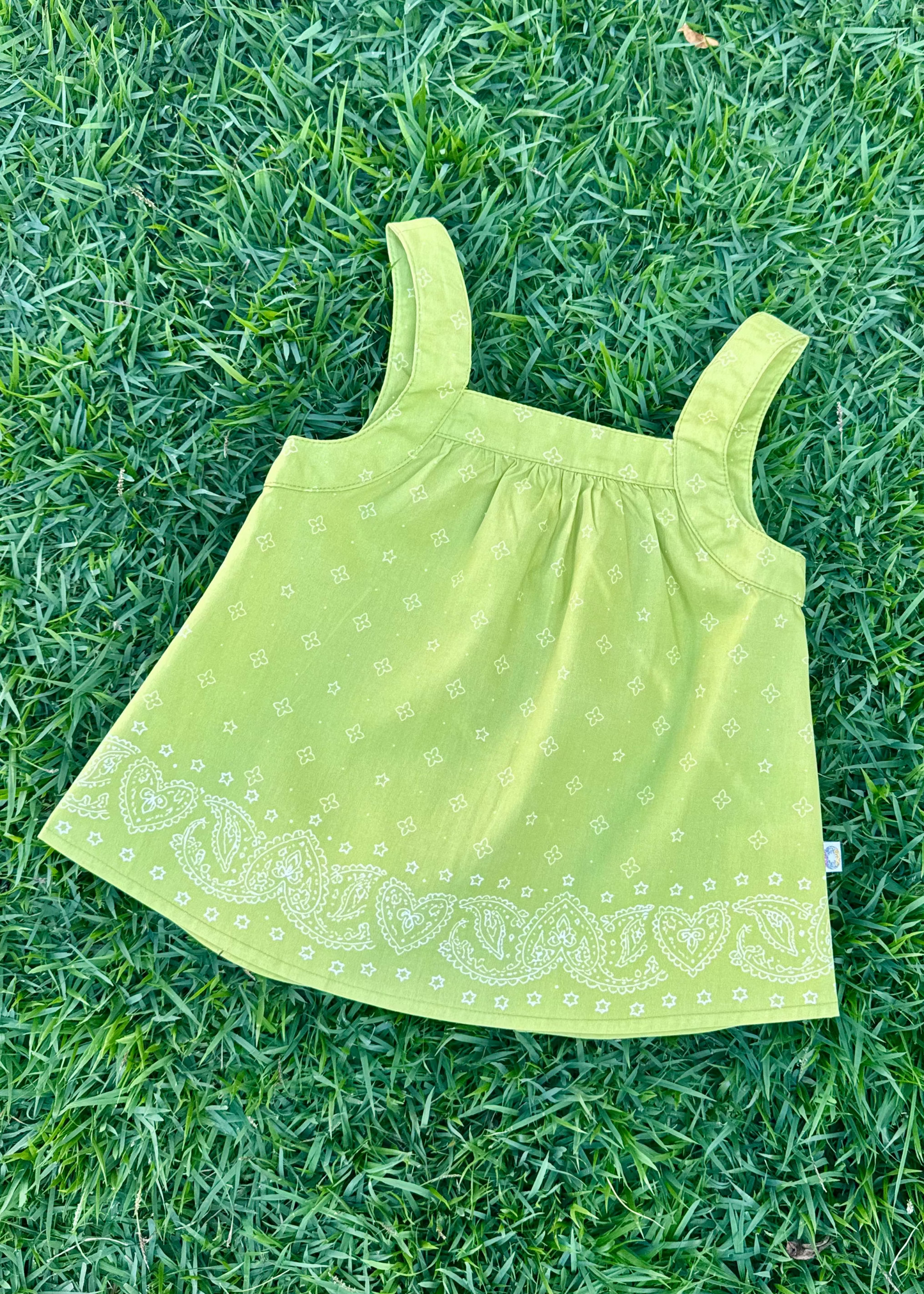 SOZO LAND Swing Top in Lime, featuring original Star Paisley print on lightweight cotton fabric, with shoulder straps, a relaxed breezy silhouette and an open-back design, photographed flat on green grass.