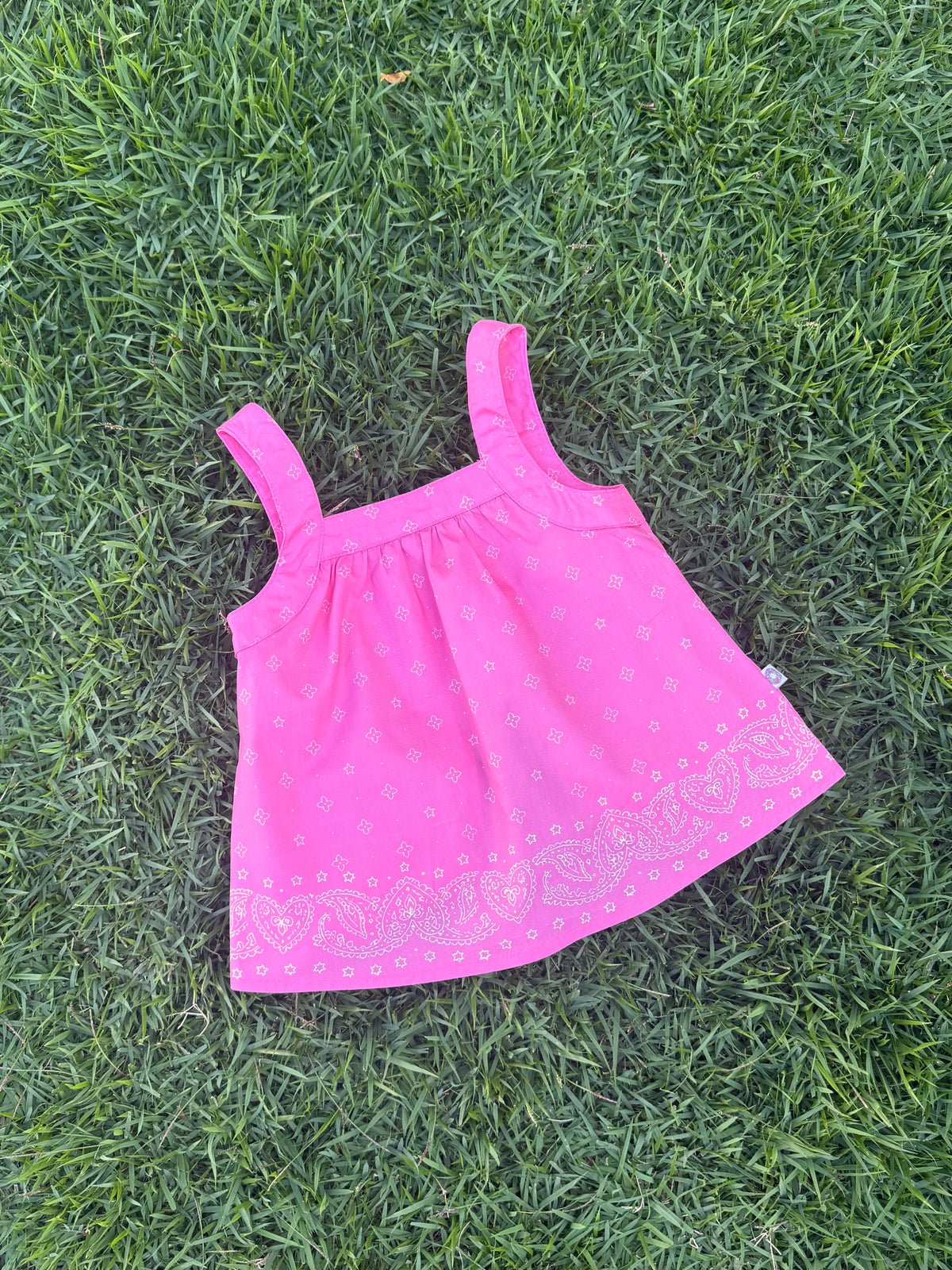 SOZO LAND Swing Top in Bubblegum pink, featuring original Star Paisley print, shoulder straps, a relaxed silhouette and an open-back design, photographed flat on green grass.