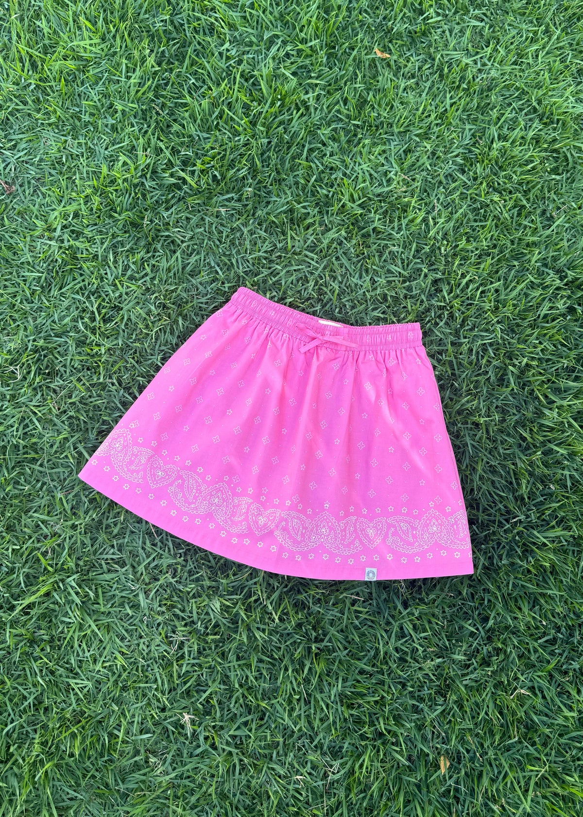 SOZO LAND Mini Skirt in Bubblegum pink, featuring our signature Star Paisley print, a soft elastic waistband, flared silhouette and built-in shorts for carefree play, photographed flat on green grass.