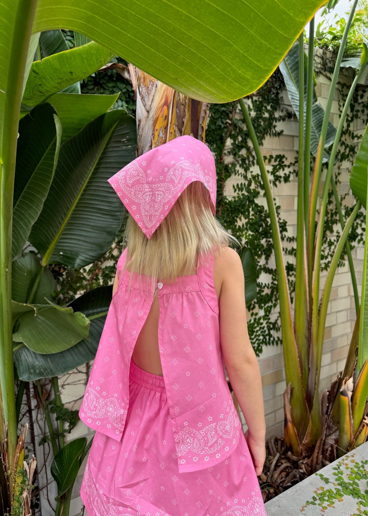 A child exploring a lush tropical garden wearing the SOZO LAND Headscarf in Bubblegum pink, featuring our signature Star Paisley print, paired with a matching pink Swing Top and Mini Skirt.