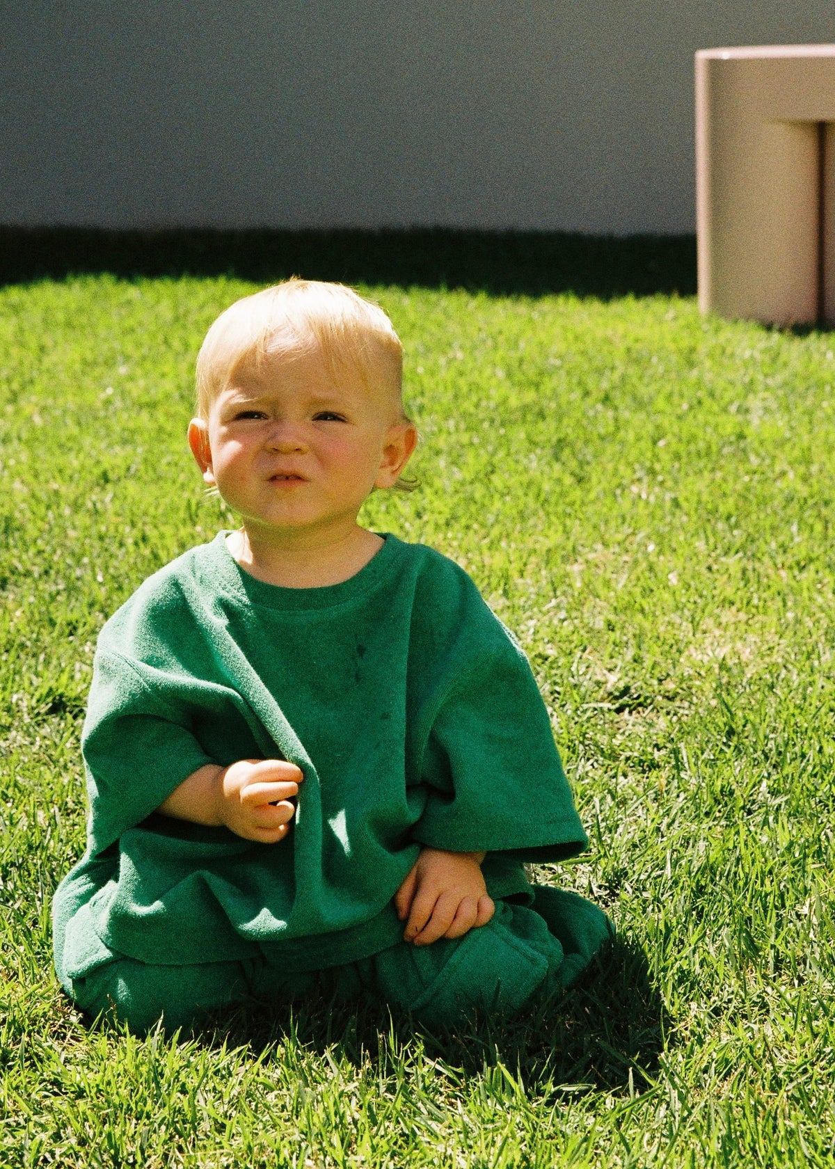 A toddler sitting on a grassy lawn outdoors wearing the SOZO LAND Terry Tee in Green , an oversized kids T-shirt made from soft cotton-blend terry, paired with matching green Terry Shorts.